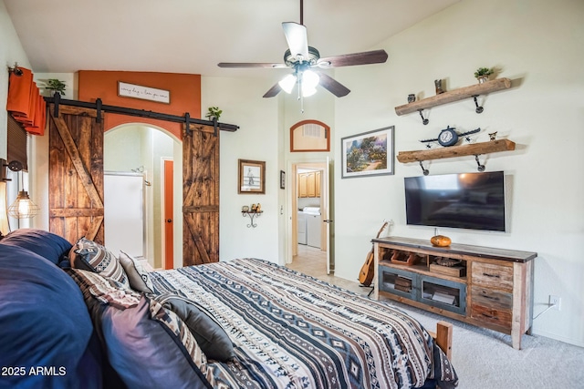 bedroom featuring ceiling fan, a barn door, light colored carpet, lofted ceiling, and washer / dryer