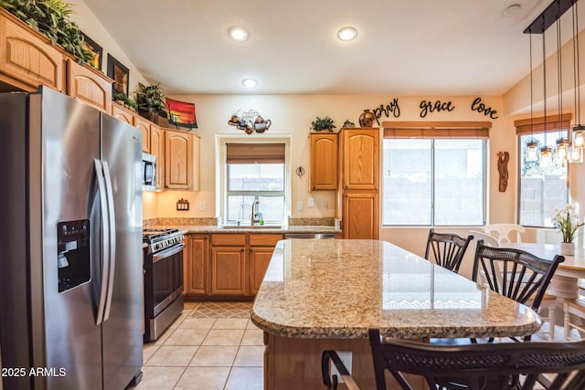 kitchen with light stone counters, stainless steel appliances, a healthy amount of sunlight, sink, and decorative light fixtures