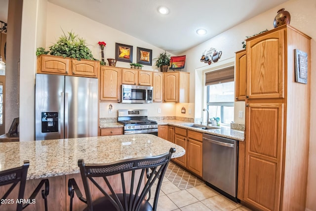 kitchen with a breakfast bar, lofted ceiling, sink, appliances with stainless steel finishes, and light stone counters