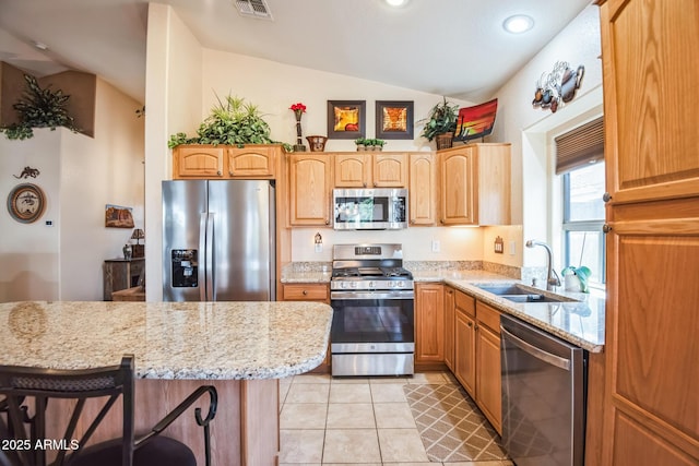 kitchen featuring lofted ceiling, a kitchen breakfast bar, sink, light stone counters, and stainless steel appliances