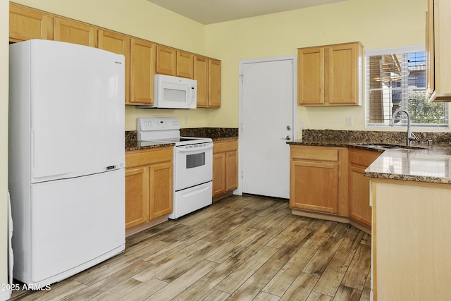 kitchen with a sink, light wood-type flooring, white appliances, and dark stone countertops