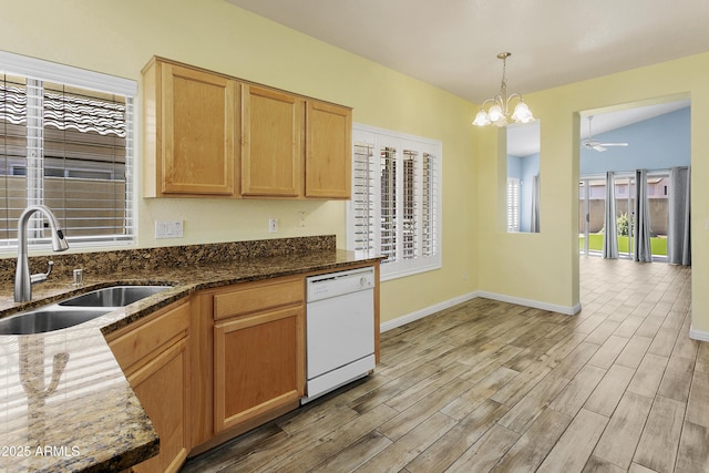 kitchen with light wood finished floors, a sink, dark stone countertops, and white dishwasher