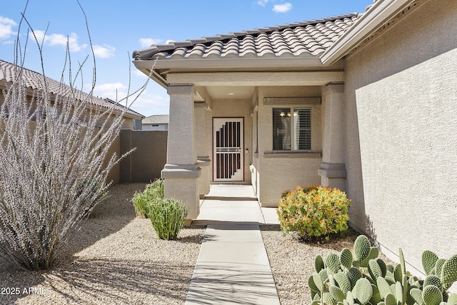 view of exterior entry with stucco siding, a tile roof, and fence