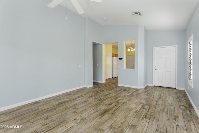 empty room featuring visible vents, baseboards, lofted ceiling, light wood-style flooring, and ceiling fan with notable chandelier