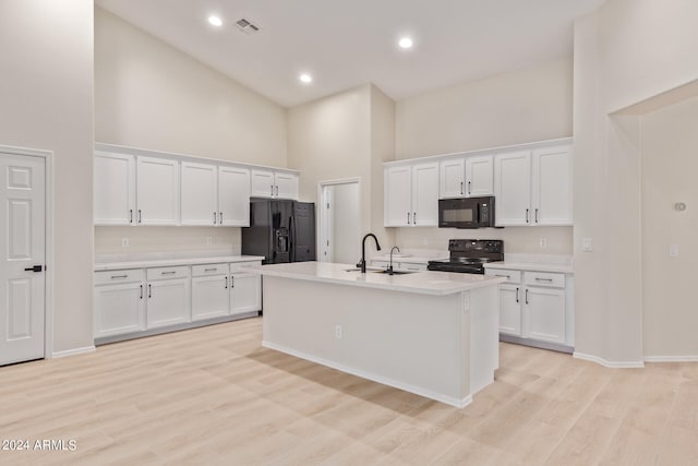 kitchen with a high ceiling, white cabinetry, black appliances, sink, and a center island with sink