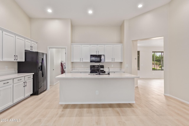 kitchen with a kitchen island with sink, black appliances, light wood-type flooring, and white cabinets