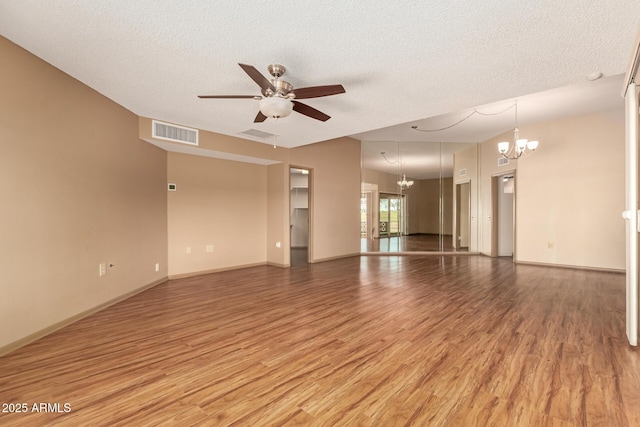 empty room featuring ceiling fan with notable chandelier, hardwood / wood-style floors, lofted ceiling, and a textured ceiling