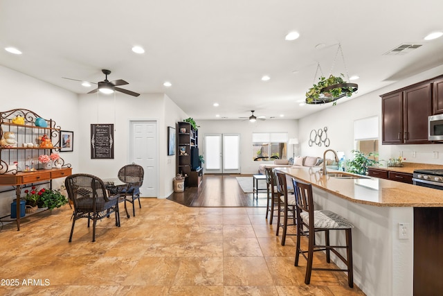 3022 E Santa Fe Ln, Gilbert, AZ 85297 - kitchen with a ceiling fan, recessed lighting, appliances with stainless steel finishes, a kitchen bar, and light stone counters