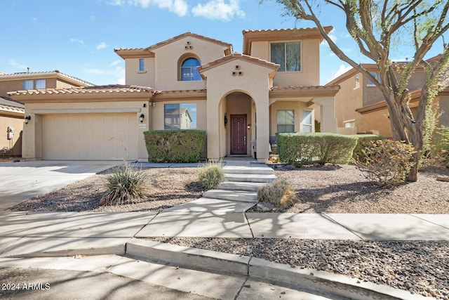 mediterranean / spanish house featuring stucco siding, a tiled roof, a garage, and driveway