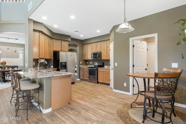 kitchen featuring appliances with stainless steel finishes, arched walkways, a sink, a peninsula, and a kitchen breakfast bar