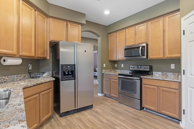 kitchen featuring appliances with stainless steel finishes, arched walkways, light wood-type flooring, light stone counters, and recessed lighting