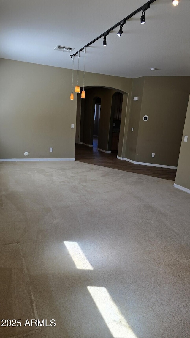 carpeted spare room featuring arched walkways and baseboards