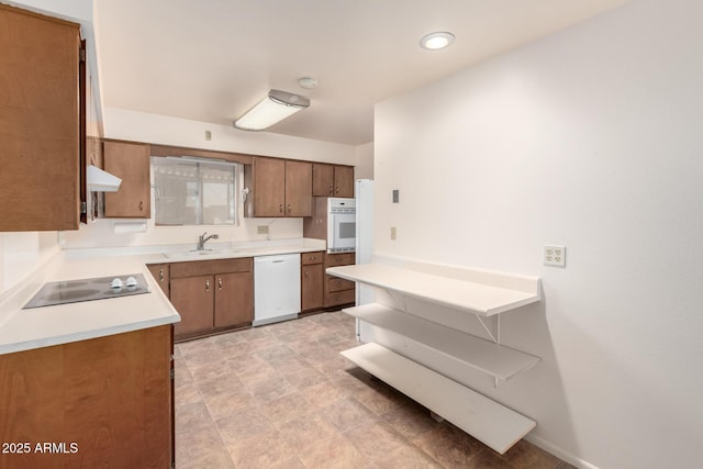 kitchen with under cabinet range hood, white appliances, a sink, light countertops, and brown cabinets