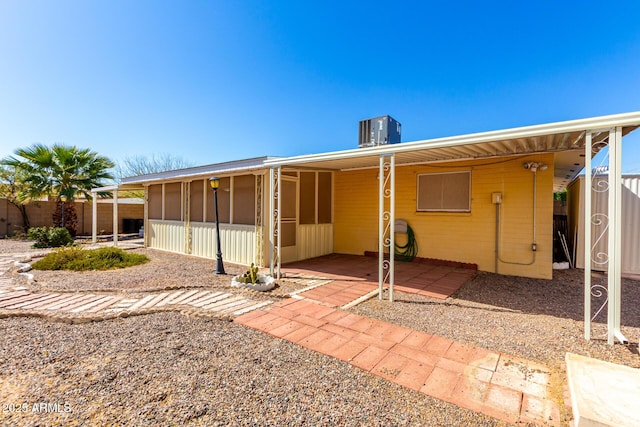 rear view of house with central AC, fence, and a sunroom