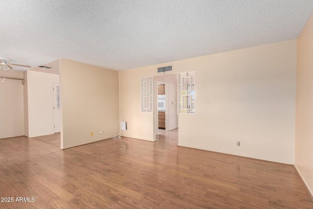 spare room with ceiling fan, a textured ceiling, visible vents, and wood finished floors