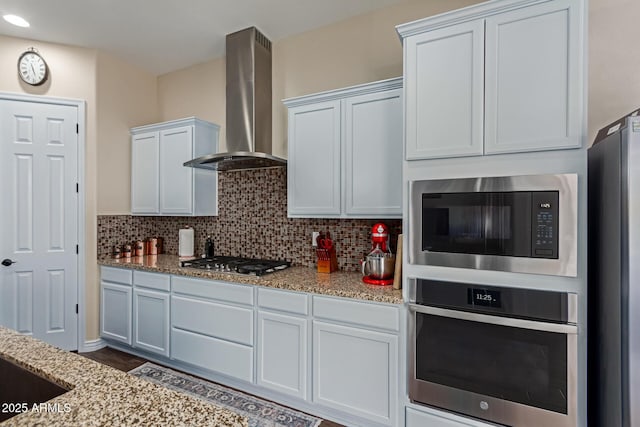 kitchen featuring white cabinetry, light stone counters, wall chimney range hood, and appliances with stainless steel finishes