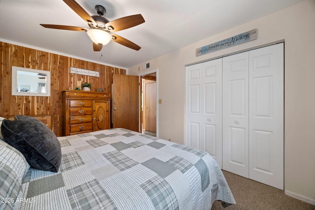 carpeted bedroom featuring visible vents, a closet, wood walls, and a ceiling fan
