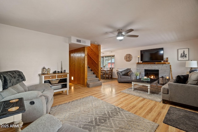 living room with stairway, visible vents, a ceiling fan, a glass covered fireplace, and wood finished floors