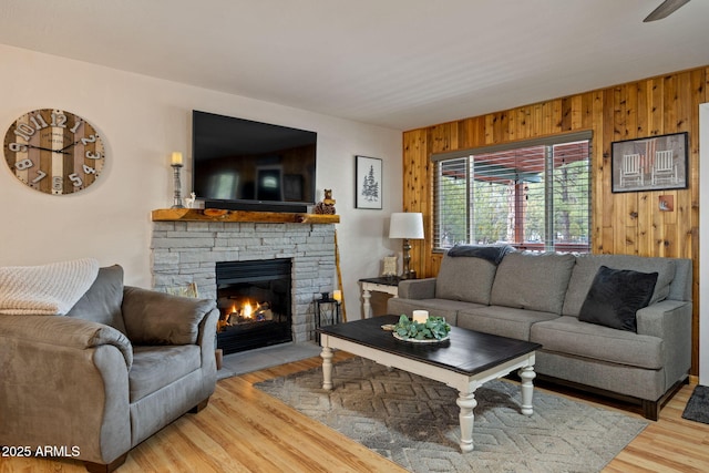living room featuring wood walls, wood finished floors, and a stone fireplace