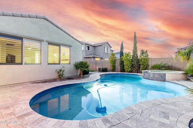 pool at dusk featuring an in ground hot tub and a patio