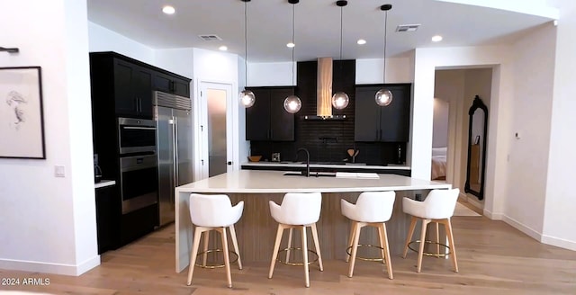 kitchen featuring a kitchen island with sink, hanging light fixtures, sink, range hood, and tasteful backsplash