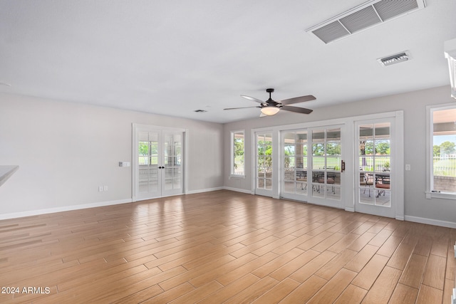 empty room featuring a healthy amount of sunlight, french doors, ceiling fan, and light hardwood / wood-style floors