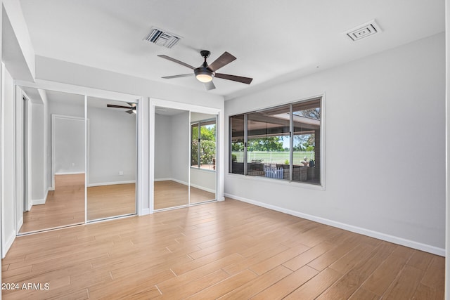 unfurnished bedroom featuring light hardwood / wood-style flooring, ceiling fan, and multiple closets