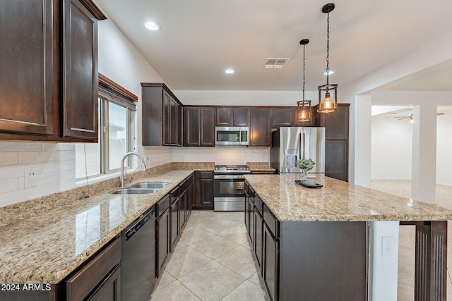 kitchen featuring stainless steel appliances, a center island, light stone counters, sink, and decorative light fixtures