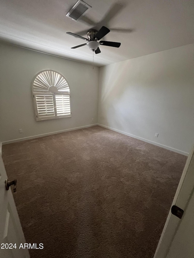 empty room with dark colored carpet, a ceiling fan, visible vents, and baseboards