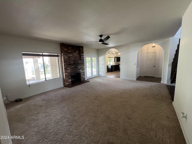 unfurnished living room featuring carpet floors, arched walkways, a ceiling fan, a brick fireplace, and baseboards