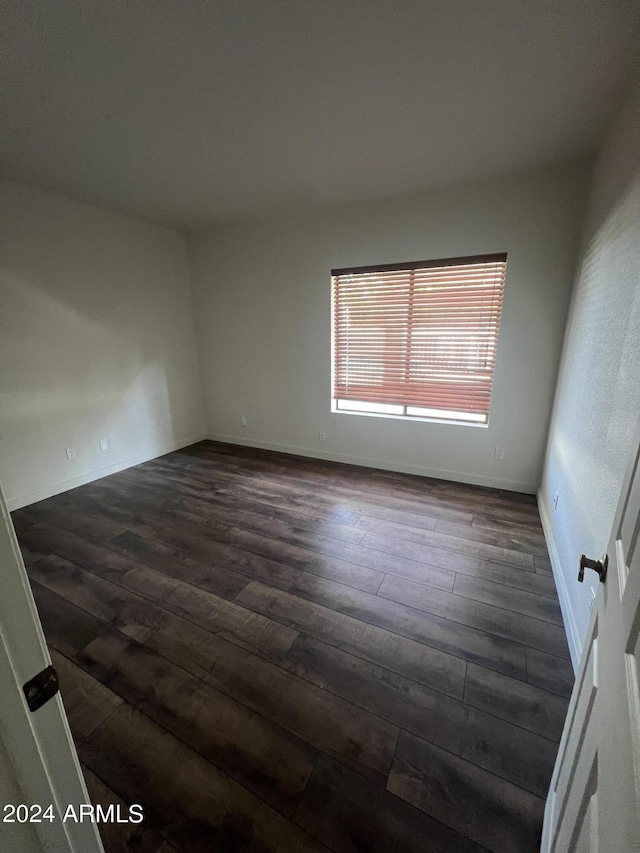 spare room featuring dark wood-style flooring and baseboards