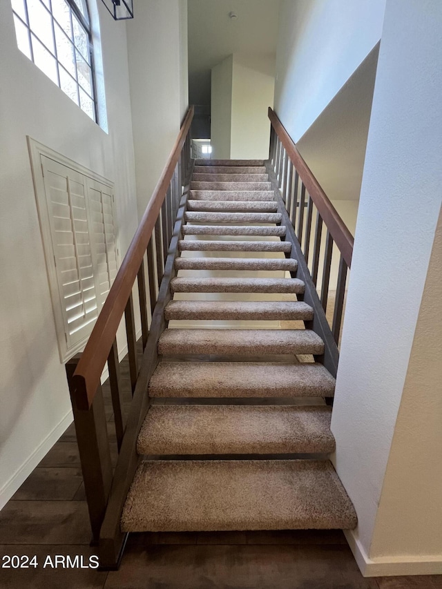 stairway with a high ceiling, baseboards, and wood finished floors