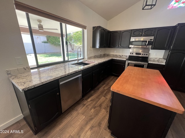 kitchen featuring dark wood-style floors, appliances with stainless steel finishes, light stone countertops, vaulted ceiling, and a sink