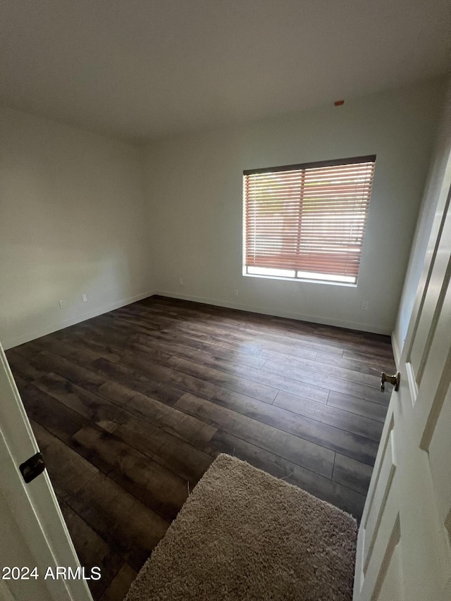 spare room with baseboards and dark wood-type flooring