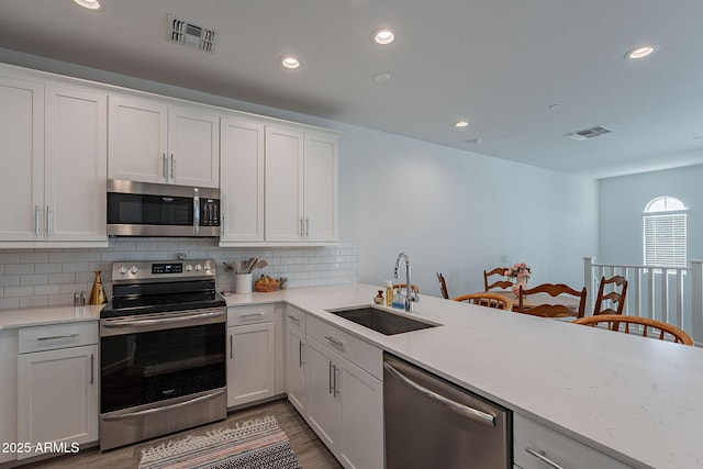 kitchen with white cabinets, stainless steel appliances, sink, backsplash, and hardwood / wood-style flooring