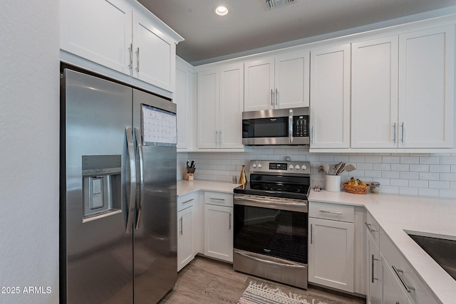 kitchen featuring light wood-type flooring, white cabinets, backsplash, and stainless steel appliances