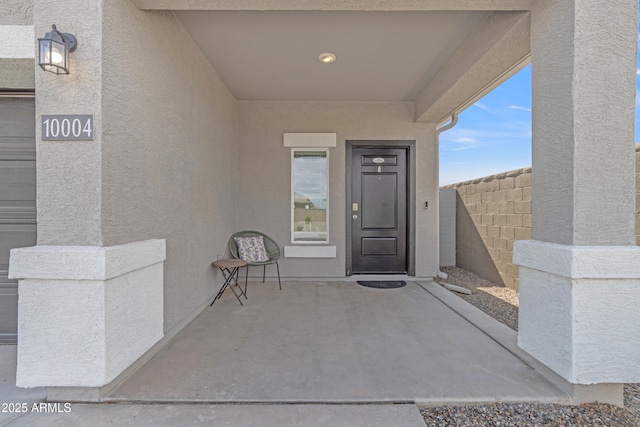 view of exterior entry with a patio, fence, and stucco siding