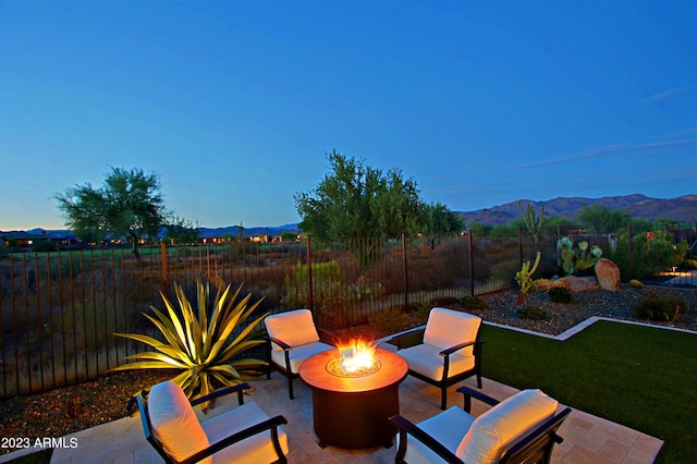 patio terrace at dusk with an outdoor fire pit, a lawn, and a mountain view