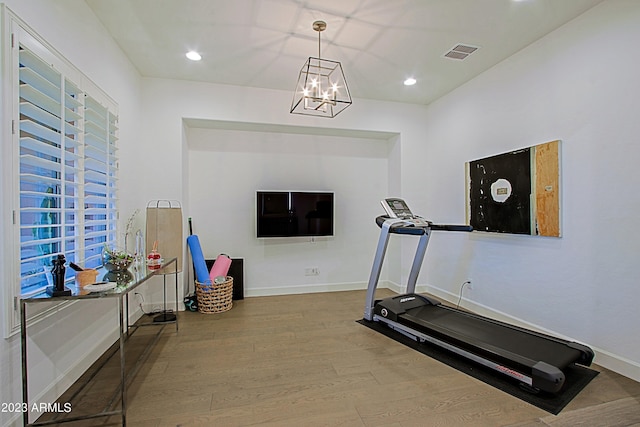 exercise room with an inviting chandelier and light hardwood / wood-style flooring