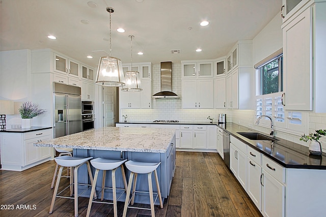 kitchen with pendant lighting, wall chimney range hood, a kitchen island, built in appliances, and white cabinetry