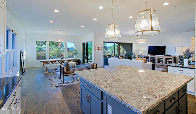 kitchen with light stone counters, dark wood-type flooring, a kitchen island, and decorative light fixtures