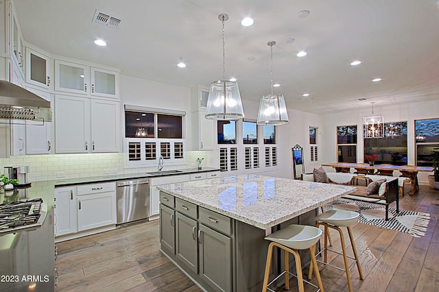 kitchen with stainless steel dishwasher, pendant lighting, light wood-type flooring, a center island, and white cabinets