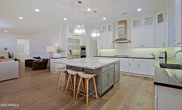 kitchen featuring built in appliances, a center island, hardwood / wood-style floors, wall chimney exhaust hood, and sink