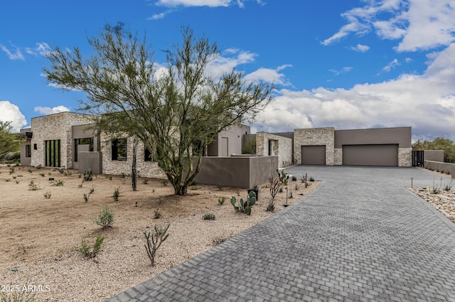 view of front of home featuring stucco siding, a garage, stone siding, a fenced front yard, and decorative driveway