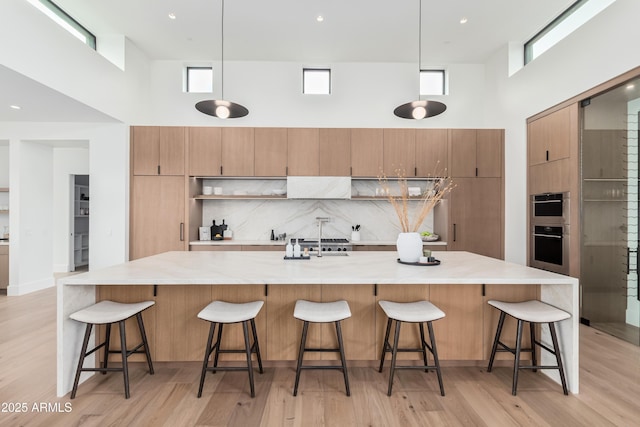 kitchen featuring a spacious island, a high ceiling, light wood-style flooring, decorative backsplash, and pendant lighting