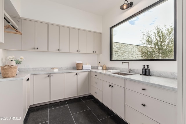 kitchen with a sink, light stone countertops, dark tile patterned flooring, and white cabinetry