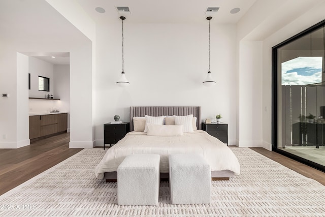 bedroom with wood finished floors, visible vents, a towering ceiling, and baseboards