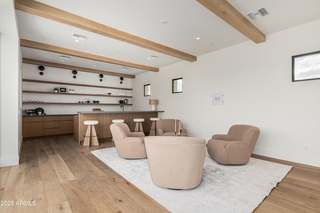 living area with beam ceiling, visible vents, and light wood-style floors