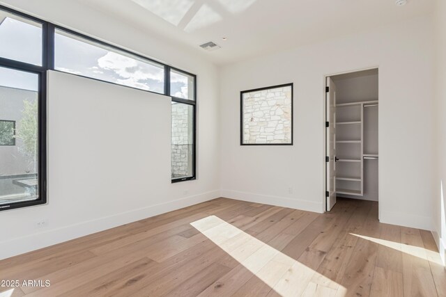 unfurnished bedroom featuring a walk in closet, baseboards, visible vents, and light wood finished floors