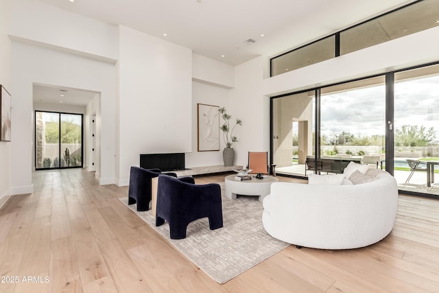 living area with a towering ceiling, visible vents, baseboards, and light wood finished floors